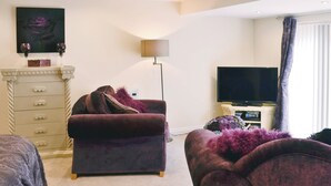 Un salon avec un canapé, un téléviseur, une lampe et une commode.