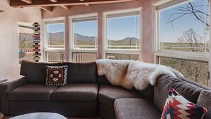 A cozy room with a sofa, a stack of books, and large windows offering a view of the outdoors. - Heavenly Mountain Views-Close to Plaza, Hot tub, Ski & Pickleball, Upscale home (Santa Fe)