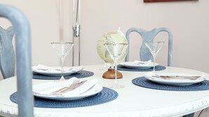 Ein runder Esstisch mit weißer Tischdecke, blauen Untersetzern und zwei leeren Weingläsern. Auf dem Tisch stehen ein Globus und ein Holzobjekt.