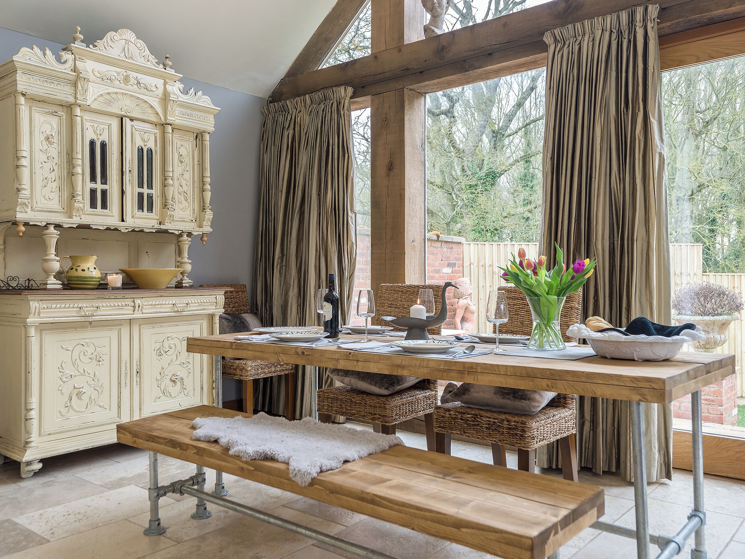 Un coin repas avec une table en bois dressée pour deux personnes, un banc et un buffet décoratif aux motifs complexes.