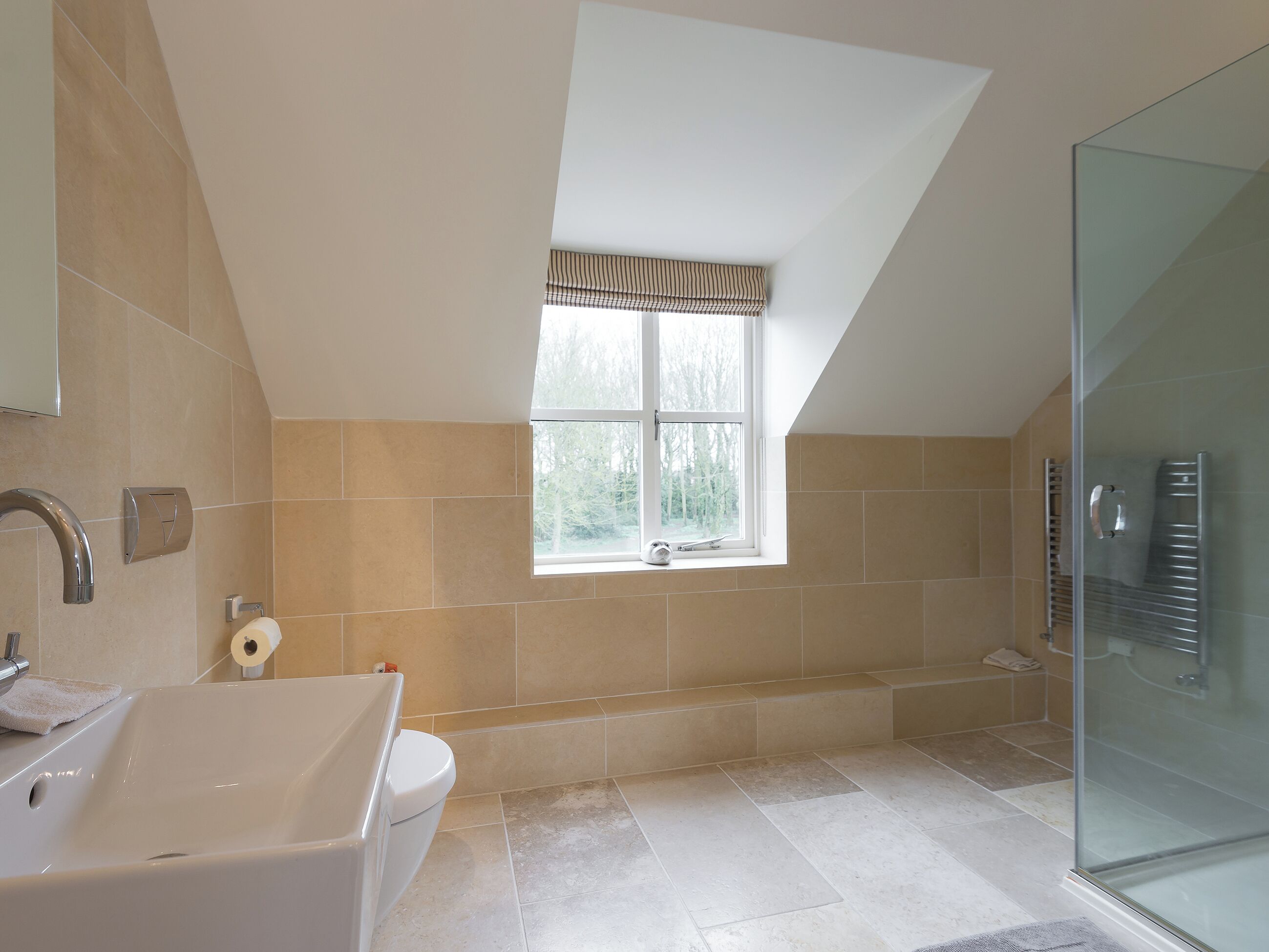A modern bathroom with a bathtub, a glass shower enclosure, and a window with a striped valance.