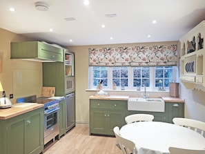 A kitchen with green cabinets, a microwave, an oven, a sink, and a window with floral curtains.