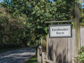 A sign reading 'Freshwater Barn' mounted on a metal post with a wooden fence in the background.