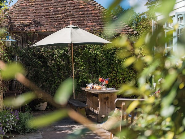 A wooden table with a bench, a large umbrella, and a brick wall in the background.