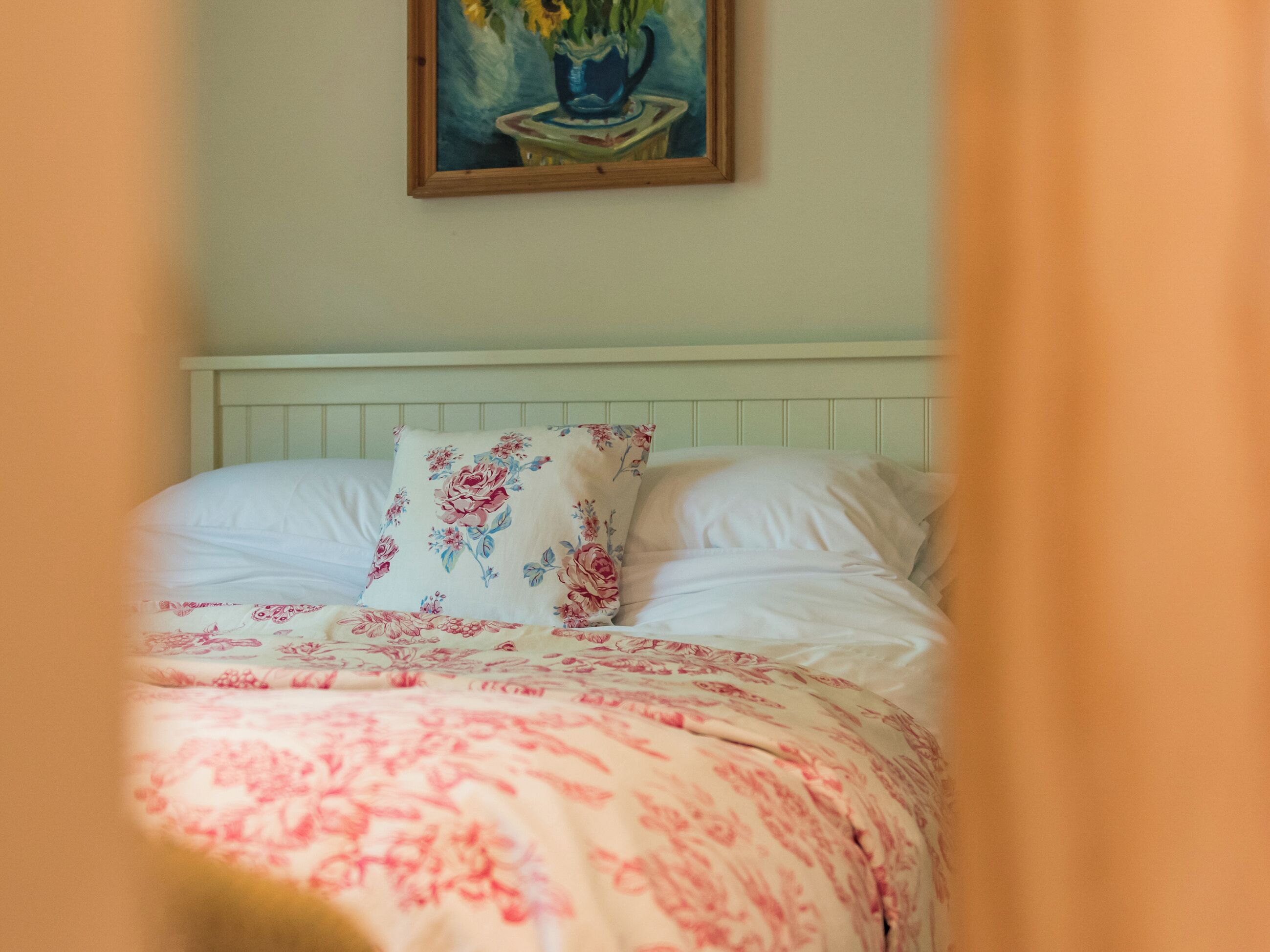 A bed with floral bedding, a painting above it, and a white headboard.
