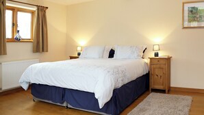 Un dormitorio con cama, dos mesitas de noche, una ventana con cortinas, un radiador, una viga de techo de madera y una lámpara colgante.