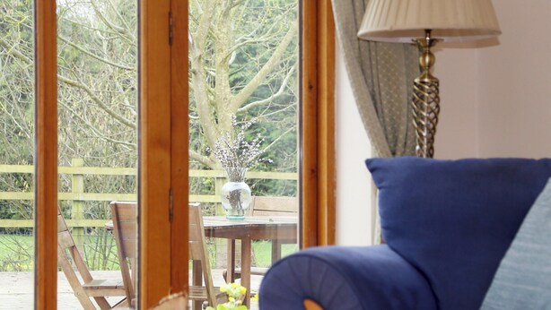 Una habitación con un sofá azul, una mesa de madera con sillas y una ventana con vistas a árboles y una valla.