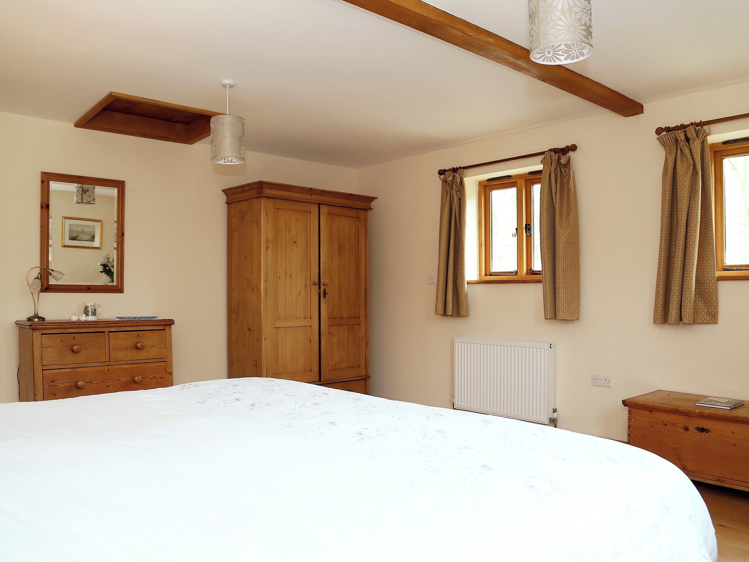 A bedroom with a bed, wooden wardrobe, a radiator, and a window with curtains.