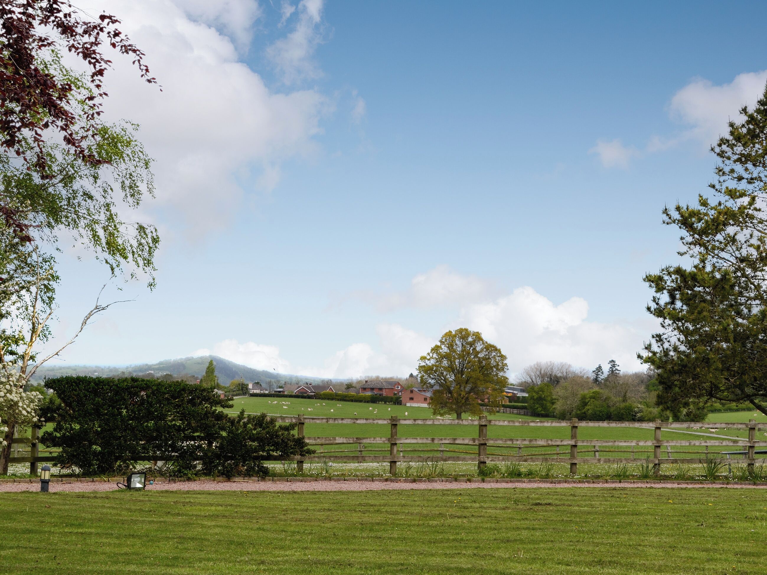 A rural landscape with a wooden fence, green fields, and a distant mountain range.
