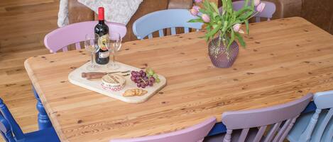 A wooden dining table with a bottle of wine, glasses, cheese, grapes, and a vase of flowers.