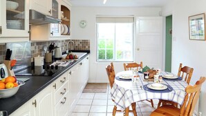 Una cucina ben illuminata con mobili bianchi, un piano di lavoro nero e un'area pranzo con una tovaglia a quadri.