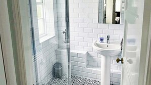Un bagno con piastrelle bianche a metro, box doccia in vetro, lavandino a piedistallo bianco e uno specchio sopra il lavandino.