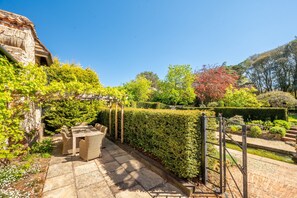 Un patio con giardino, un tavolo e sedie, un muro in pietra e un siepe.