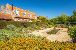 Un bâtiment historique doté d’un toit recouvert de tuiles, d’un jardin avec un bassin et d’une haie bien entretenue.
