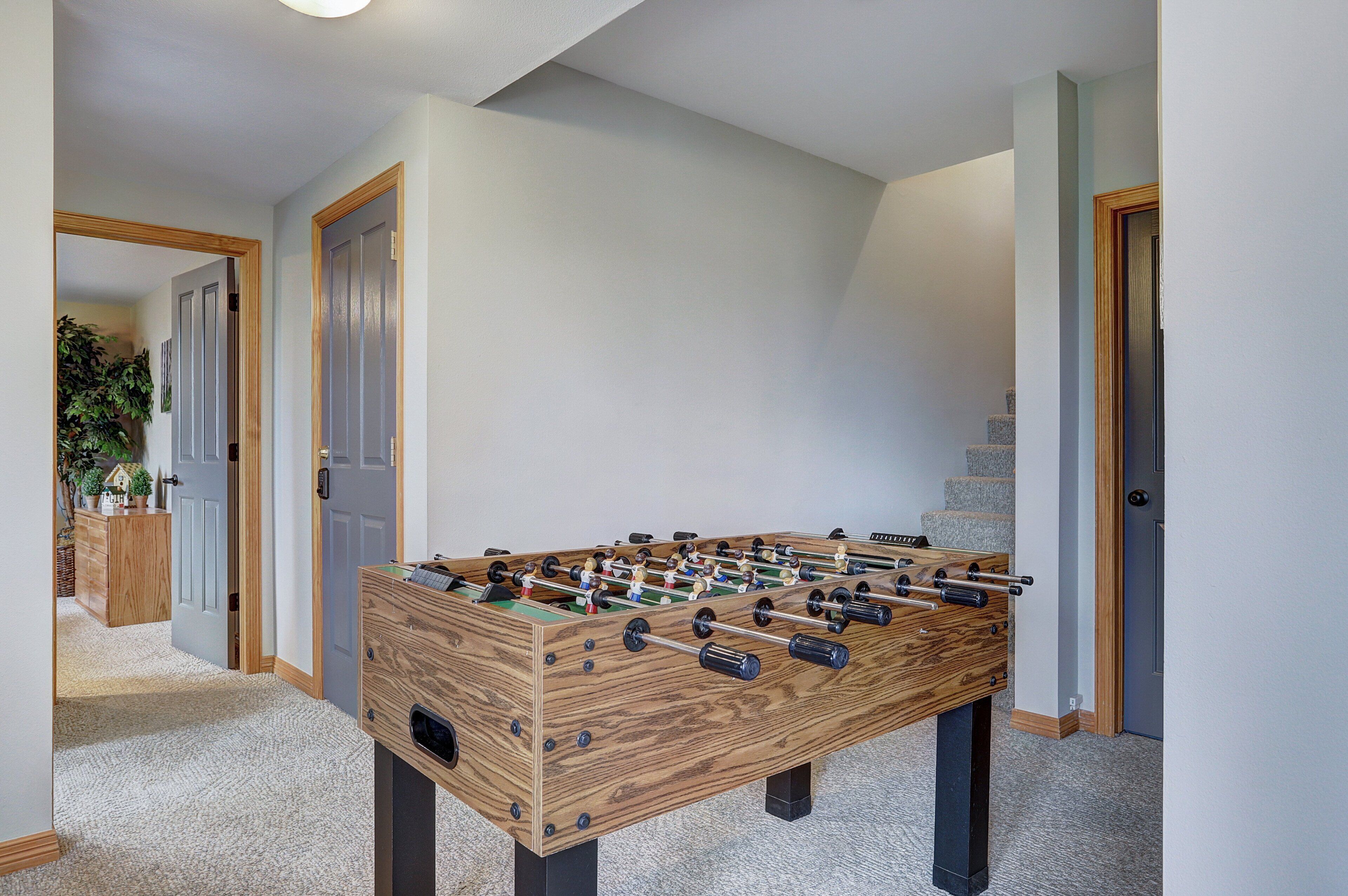 Une table de baby-foot en bois se trouve dans un couloir, dont le sol est recouvert de moquette et les murs sont de couleur claire.