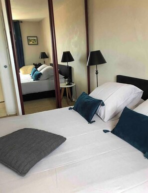 Una habitación de hotel con una cama, dos lámparas de noche, una mesita y un cuadro en la pared.