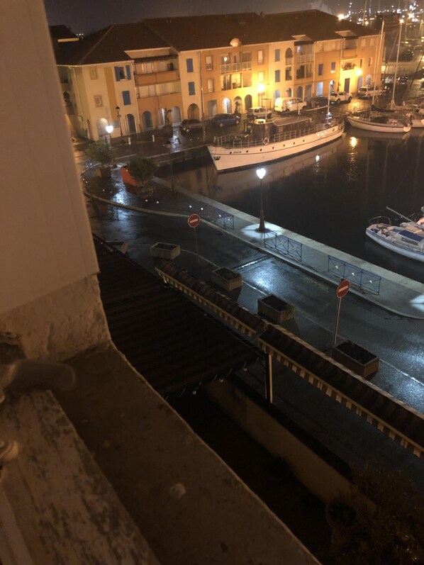 A nighttime view of a waterfront area with buildings, a boat docked at the pier, and a no-entry sign on the road. - Apartment with marina and sea view (Port de bouc)