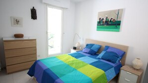 Un dormitorio con cama, mesita de noche, cómoda y un cuadro en la pared.