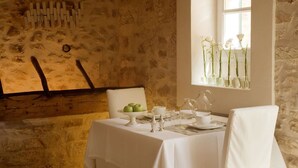 A dining area with a table set for two, a rustic stone wall, and a window with flowers. - S'Hotelet de Santanyi (Santanyi)