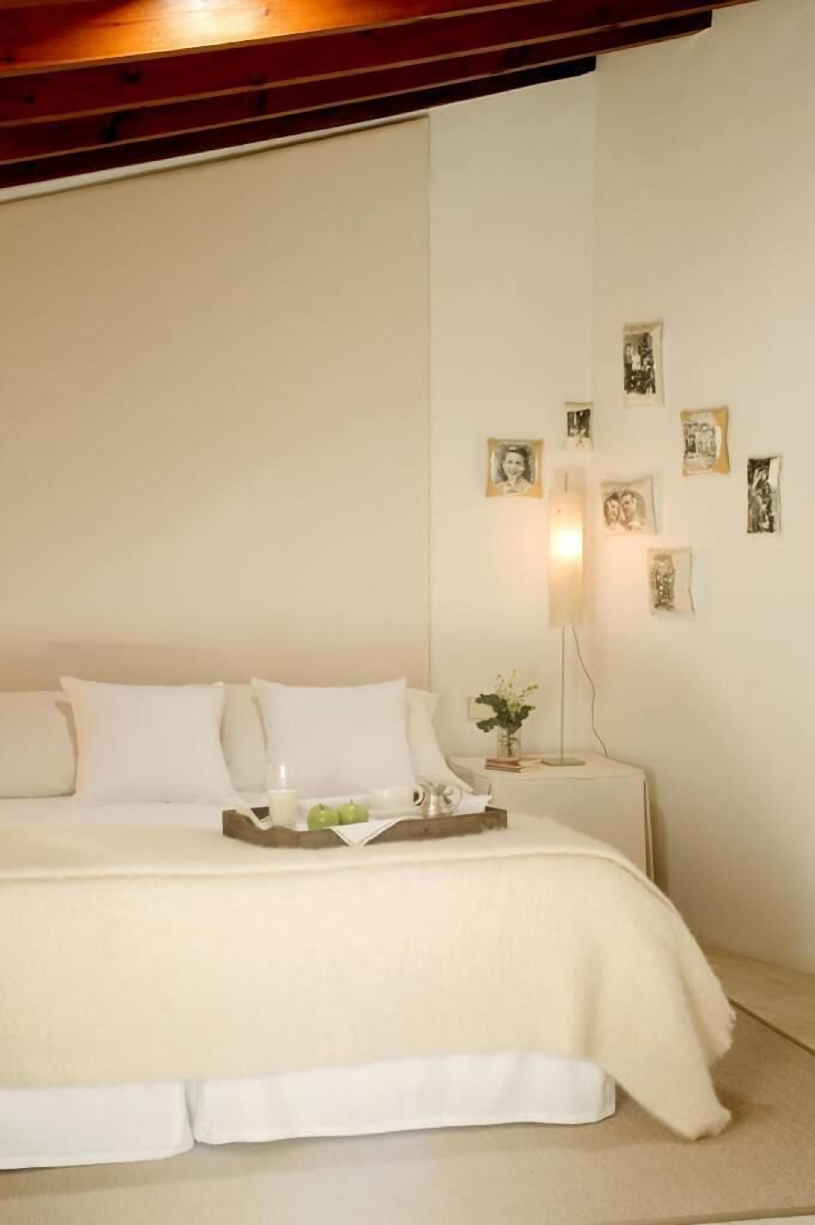 A neatly made bed with a white bedspread, a bedside table with a lamp, and several framed pictures on the wall.