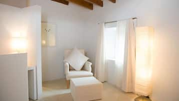 Una habitación minimalista con un sillón blanco, un pequeño reposapiés, una lámpara de pie y una ventana con cortinas.