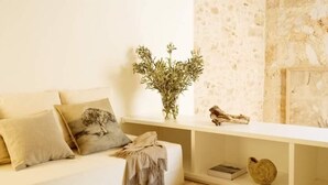 A minimalist living room with a white sofa, a vase with greenery, and a stone wall. - S'Hotelet de Santanyi (Santanyi)