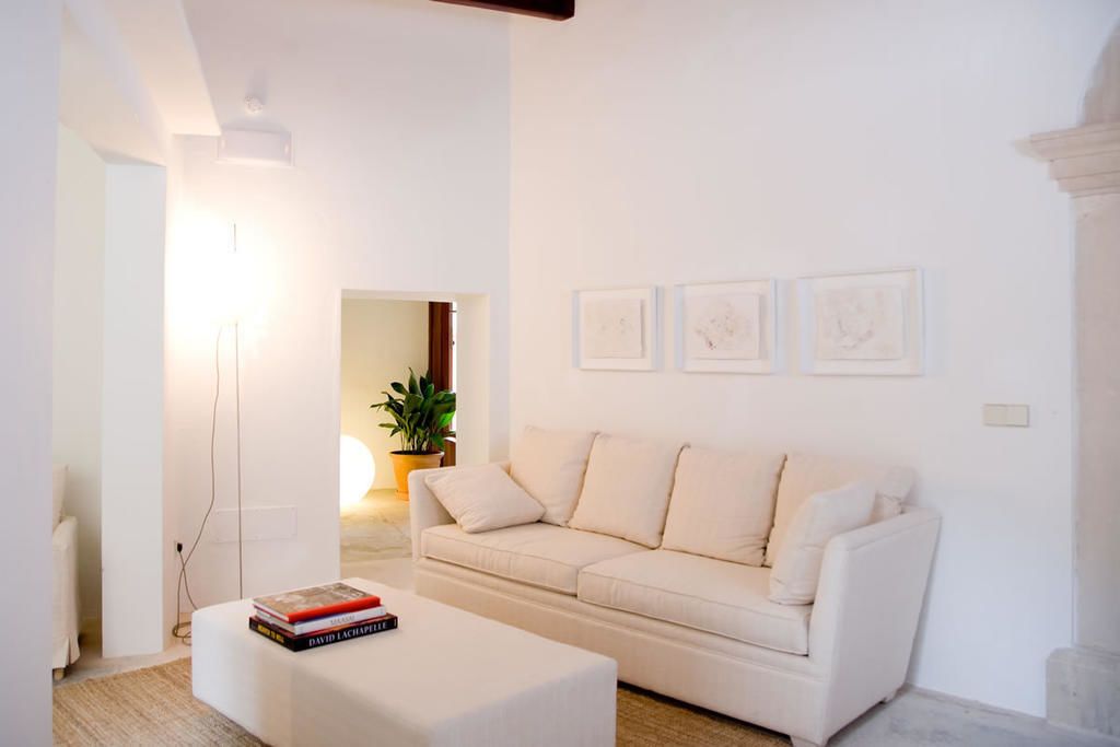 Una sala de estar moderna con un sofá blanco, un pequeño reposapiés blanco y tres obras de arte enmarcadas en la pared.