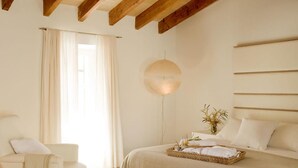 A bedroom with a bed, a bedside table, a lamp, and a window with curtains. - S'Hotelet de Santanyi (Santanyi)