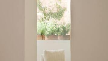 A room with a white chair, a small table with a vase of flowers, and a view of a garden through a window.