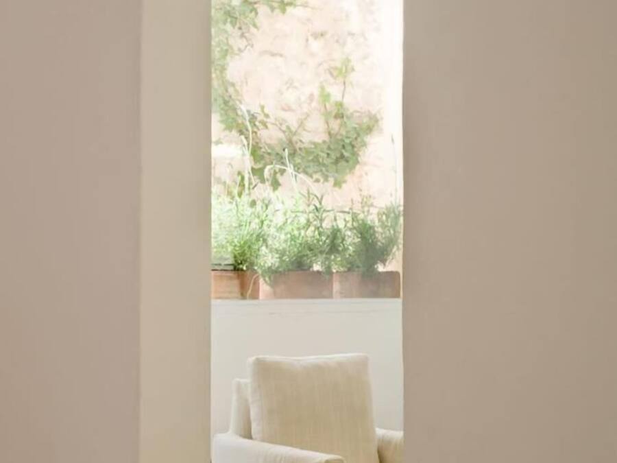 A room with a white chair, a small table with a vase of flowers, and a view of a garden through a window.
