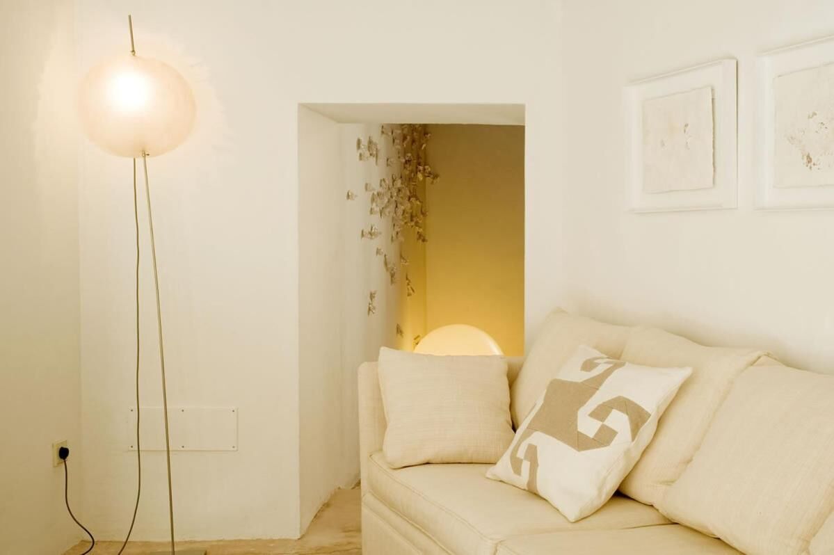 A room with a floor lamp, a sofa with cushions, and a wall-mounted light fixture.