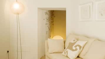 A room with a floor lamp, a sofa with cushions, and a wall-mounted light fixture.