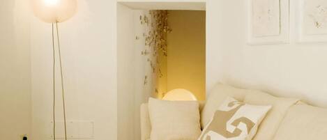 A room with a floor lamp, a sofa with cushions, and a wall-mounted light fixture.