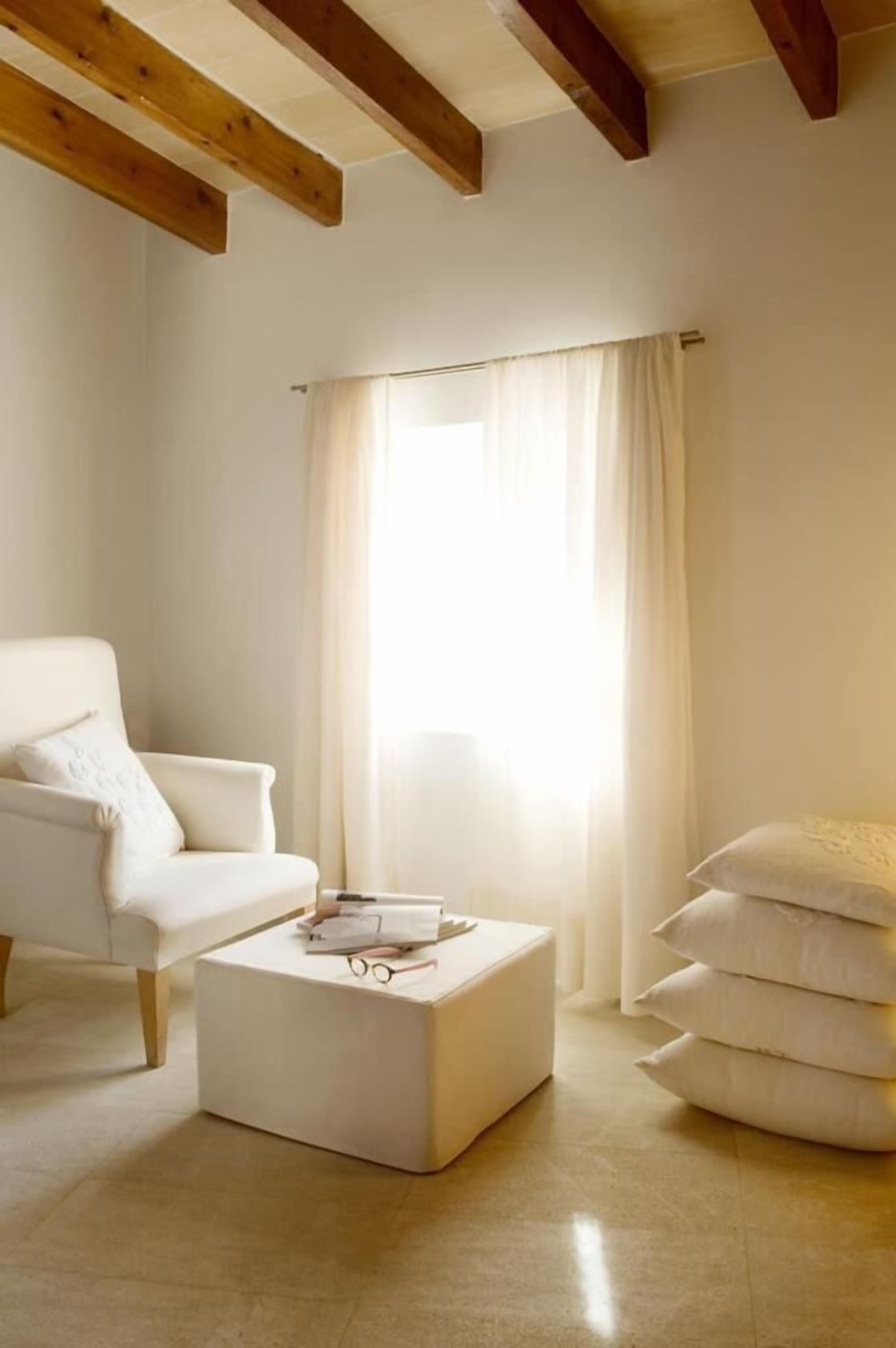 A minimalist living room with a white sofa, a white coffee table, and a large window with sheer curtains.