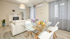 A modern living room with a glass dining table, white sofa, and a TV on a stand. - 50 meters from the lake, in the historic center with a terrace. Stella House (Desenzano del Garda)