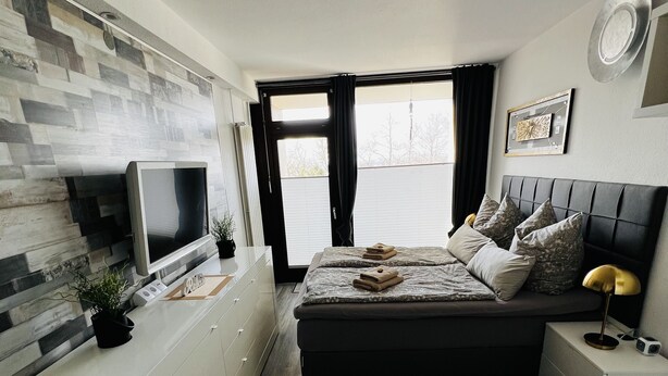Ett modernt sovrum med en säng, ett nattduksbord, en tv och ett skrivbord med en dator.