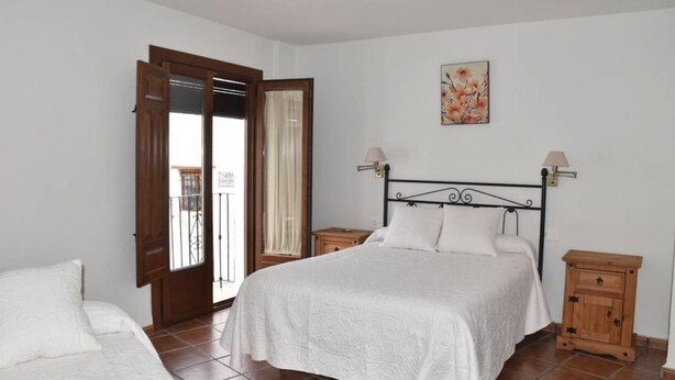 A bedroom with a bed, two bedside tables, a nightstand, a door, and a window with curtains. - VISTA VELETA CASA ROMERO (Capileira)
