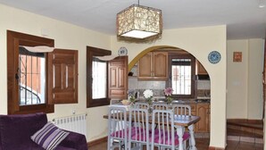 A cozy living room with a purple sofa and a dining area with white chairs and a wooden table. - VISTA VELETA CASA ROMERO (Capileira)