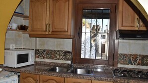 A kitchen with wooden cabinets, a microwave, a sink, and a stove. - VISTA VELETA CASA ROMERO (Capileira)