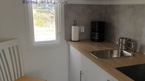 Una cocina compacta con ventana, una silla, cafetera y lavamanos.