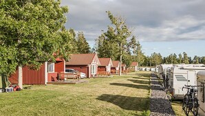 Un camping con vehículos recreativos estacionados en filas, un edificio rojo con porche y un área verde con árboles.