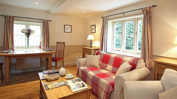 A cozy living room with a wooden coffee table, a sofa with a red and white checkered blanket, a dining table with chairs, and a window with curtains. - 1 bedroom accommodation in Tunbridge Wells (Tunbridge Wells)