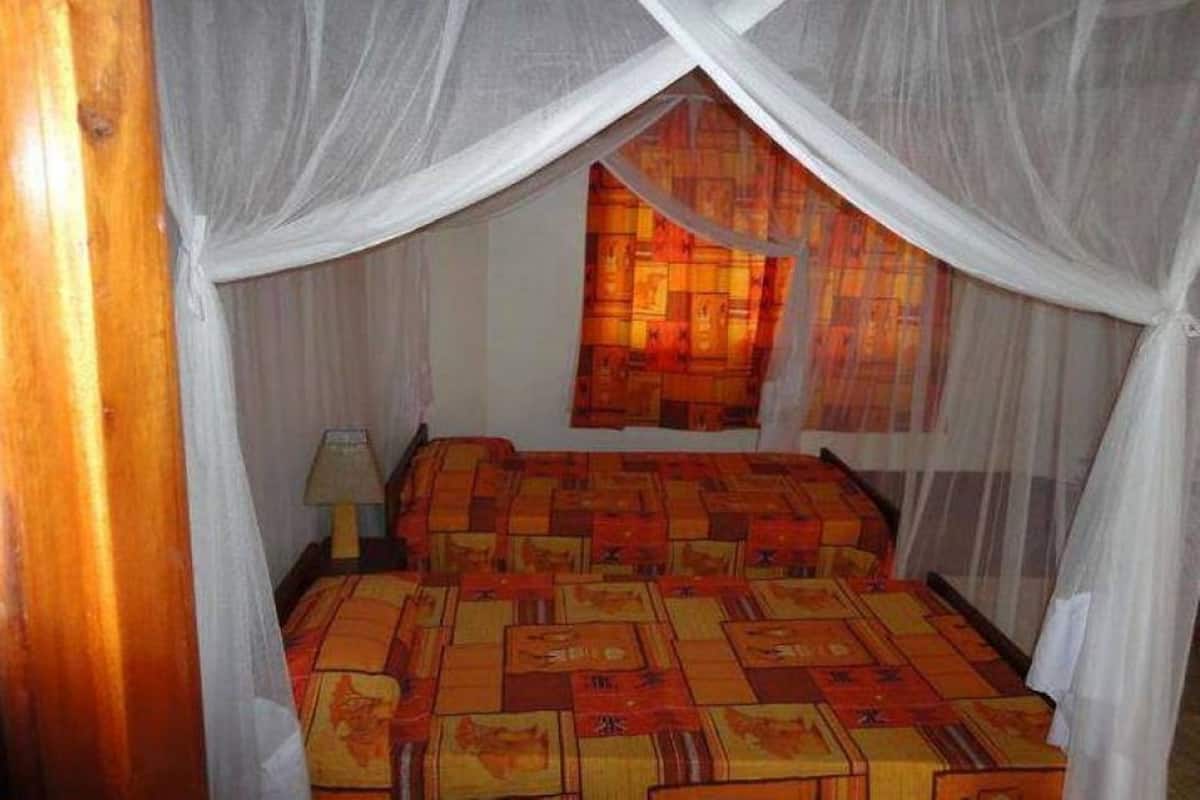 A room with a bed covered by a patterned bedspread, a nightstand with a lamp, and a window with a curtain.