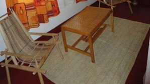 A room with a woven mat, two wooden chairs, a wooden table, and patterned curtains. - Bwana Tembo Safari Lodge (Pakwach)