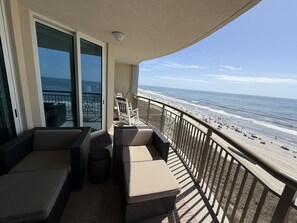 A balcony with wicker furniture, a glass door leading to a balcony, and a view of the beach. - MVG 911 3 Bedroom 3 Bath  Oceanfront (North Myrtle Beach)