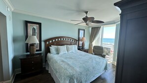 Een slaapkamer met een bed, twee nachtkastjes, een plafondventilator en uitzicht op de oceaan.