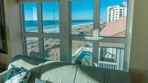 Een kamer met een groot raam met uitzicht op een strand en een gebouw.
