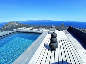 A wooden deck with a clear blue pool, lounge chairs, and a view of the sea and mountains. - ArtHouse (Marathon)