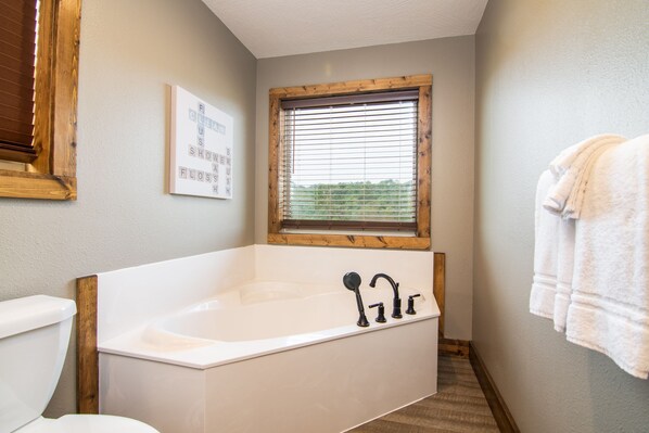 A bathroom with a bathtub, a window with blinds, a toilet, and a towel rack.