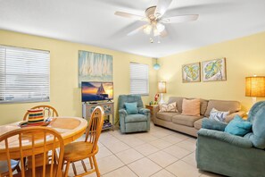 A living room with a dining area, a ceiling fan, and artwork on the walls.